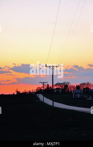 Burlington, Illinois, USA. Ein farbenfroher Sonnenuntergang läutet das Ende des Tages im Nordosten Illinois farm country über eine Landstraße. Stockfoto
