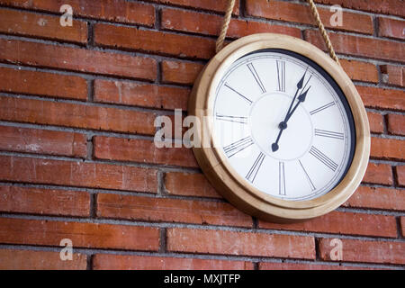 Medium in der Nähe geschossen von einem hölzernen Wanduhr mit römischen Ziffern in einem roten Backsteingebäude an der Wand hängen. Stockfoto