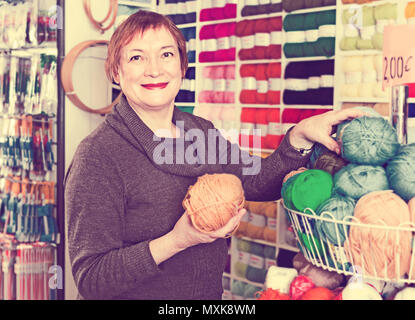 Froh, heiter positive lächelnde reife Frau kaufen bunte Garne für Ihr Hobby auf spezielle Angebote Stockfoto