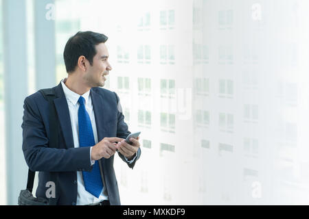 Business Mann zu Fuß und mit Handy zu chatten mit Freunden nach der Arbeit im Korridor Bürogebäude Stockfoto