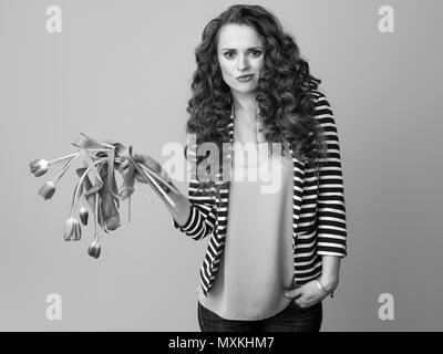 Traurige junge Frau in gestreifte Jacke im Hintergrund halten verwelkte Blumen Stockfoto