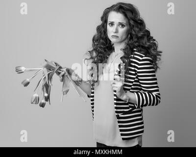 Traurige moderne Frau mit langen, welligen Brünette Haare auf Hintergrund halten verwelkte Blumen Stockfoto
