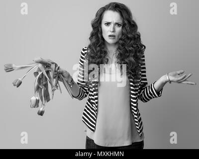 Unglücklich trendy Frau mit langen Welligen brünette Haare auf Hintergrund mit verwelkten Blumen Stockfoto