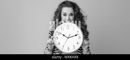 Trendy Frau in gestreifte Jacke auf Hintergrund beißen Clock betonte Stockfoto