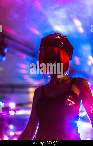 Defokussiertem Hintergrund mit bokeh Lichter in rosa violett Farben in einer Disco Club mit Tanzen Frau in polizistin Kleid und rote Perücke. Stockfoto