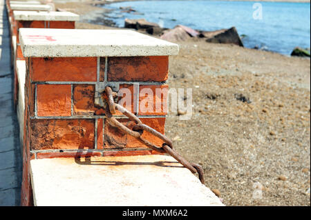 Starke, kräftige, rostige Kette Schuß im Sonnenlicht. Schatten von der Kette. Brick Zaun und das Meer. Stockfoto