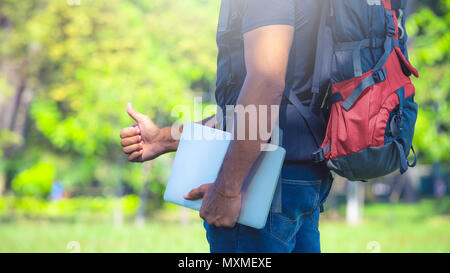 Mann mit einem Rucksack in einem Park während der Tag. Backpacker Holding einen Laptop. Digital nomad Konzept Stockfoto