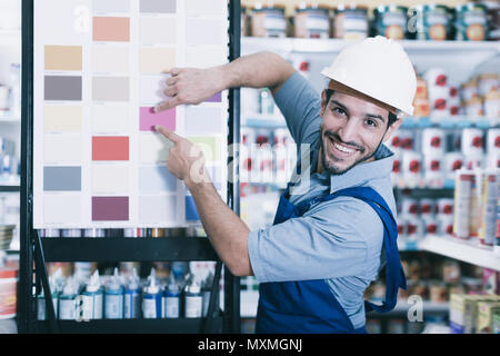 Lächelnd Vorarbeiter in blauen Overalls mit Proben von Farbe auf Stand in Store Stockfoto