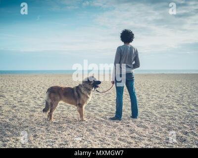 Ein junger Mann steht am Strand mit seinem Leonberger Hund Stockfoto