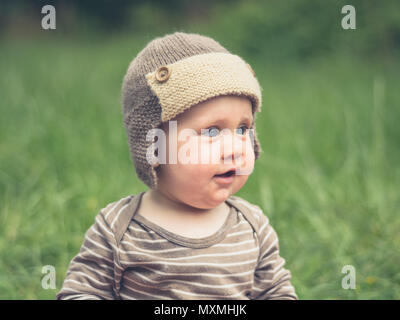 Ein süßes kleines Baby ist draußen in der Natur und ist mit Hut Stockfoto