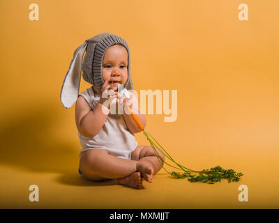 Ein süßes kleines Baby tragen ein Häschen hat ist auf dem Boden sitzend mit einer Karotte Stockfoto