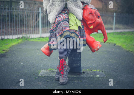 Eine Frau in grungy Kleidung sitzt auf einem Elefanten auf einem Spielplatz Stockfoto