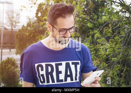 Attraktive junge lächelnde Mann mit Phone in einem öffentlichen Park Stockfoto
