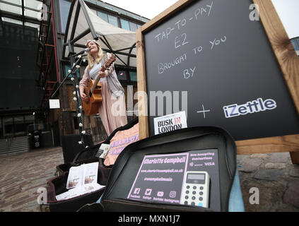 Busker Charlotte Campbell führt in Camden Market, nördlich von London, als Kate Jones, Programmdirektor bei Busk in London, schaut an. London hat erste kontaktlose Zahlung das Schema der Welt für Straßenmusikanten in Zusammenarbeit mit Technologieunternehmen iZettle gestartet. Stockfoto