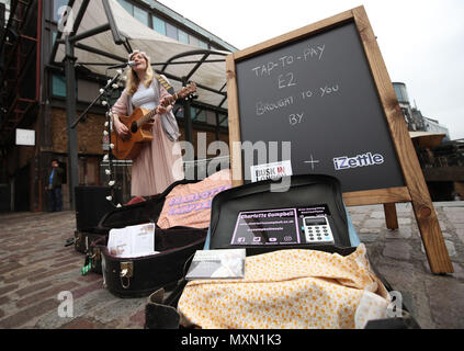 Busker Charlotte Campbell führt in Camden Market, nördlich von London, als Kate Jones, Programmdirektor bei Busk in London, schaut an. London hat erste kontaktlose Zahlung das Schema der Welt für Straßenmusikanten in Zusammenarbeit mit Technologieunternehmen iZettle gestartet. Stockfoto