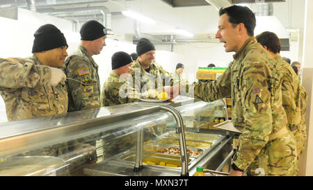 Ein Kaplan der US-Armee mit dem 2. Bataillon, 503. Infanterieregiment, 173. Luftlandebrigade, bietet einem britischen Soldaten während des Thanksgiving-Dinners am 25. November 2016 in Pabrade, Litauen, Bollard Greens an. Fallschirmjäger der Able Company, die an Übung Iron Sword 2016 teilnahmen, luden NATO-Verbündete ein, das Essen zu teilen. An der Übung beteiligen sich 11 NATO-Länder und 4.000 Soldaten, die die regionale Stabilität, die Partnerschaftsfähigkeit, das Vertrauen sowie die gemeinsame Ausbildung und Koordinierung der alliierten Streitkräfte fördern sollen. Stockfoto
