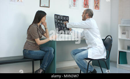Männlicher Arzt Übersicht xray Ergebnisse gesorgt zu weiblichen Patienten und beim Ausfüllen von Formularen Stockfoto