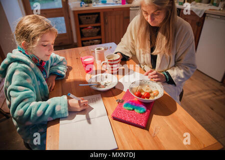 Mutter und Tochter sitzen am Tisch in der Küche. Mutter ist die Kontrolle über ihre Töchter Hausaufgaben vor der Schule. Stockfoto