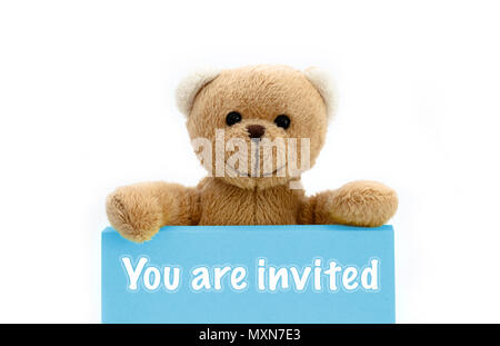 Sie sind Blue Card mit braunen Teddybär Holding mit den beiden Händen die Note mit der Botschaft eingeladen. Foto isoliert in einem nahtlosen weißen Hintergrund. Stockfoto