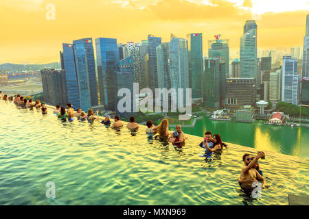 Singapur - Mai 3, 2018: Paare und Touristen nehmen selfie im berühmten Infinity Pool der Skypark, dass Tops die Marina Bay Sands Hotel. Bankenviertel Skyline im Hintergrund. Aufnahme bei Sonnenuntergang. Stockfoto