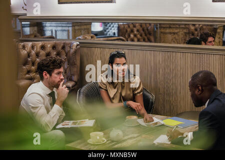 Seitliche Sicht auf drei Personen, die ein kleines Geschäft treffen und reden über etwas Kaffee. Stockfoto