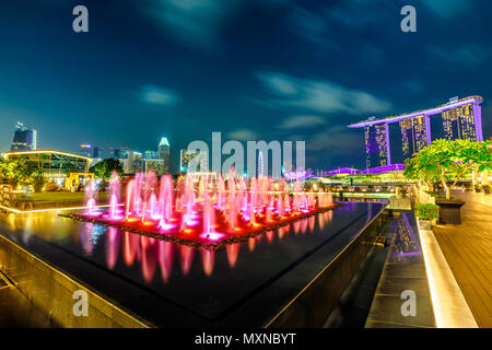 Singapur - 28. April 2018: Weitwinkelaufnahme der Brunnen in der Nähe der bunten Fullerton Fullerton Bay Hotel, Clifford Platz in der Marina Bay Walkway Promenade. Lasershow im Marina Bay Sands an der blauen Stunde. Stockfoto