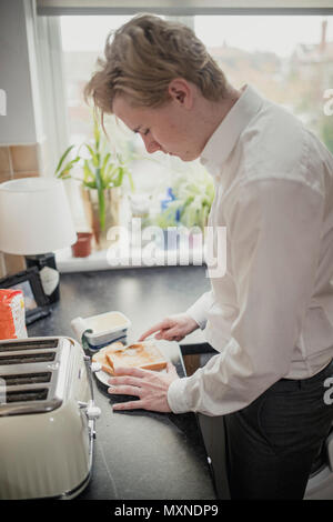 Close-up, seitliche Betrachtungswinkel eines jungen Erwachsenen Geschäftsmann machen Toast für sein Frühstück vor der Arbeit. Stockfoto