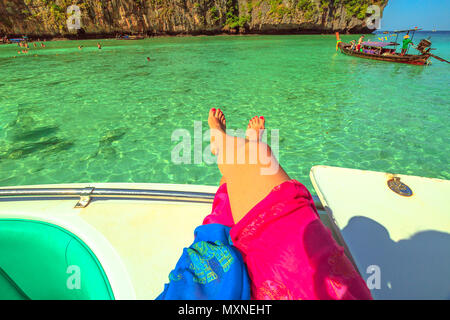 Frau gebräunte Beine auf einem touristenboot im tropischen und idyllischen Lagune des beliebten Maya Bay, Ko Phi Phi Leh in Phi Phi Island, Krabi, Andaman Meer. Urlaub, Lifestyle und Sonnenbaden Konzept. Stockfoto