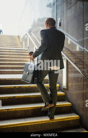 Rückansicht eines junge Unternehmer zu Fuß die Treppen hinauf in den trian Station auf seinen Morgen pendeln. Stockfoto