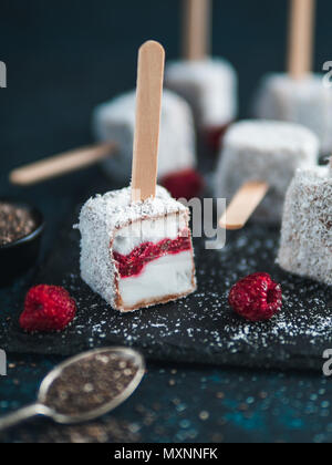 Hausgemachte raw lamington Eis erscheint auf dunklem Hintergrund. Australische süße Nachspeise lamington mit Chia und Himbeeren Marmelade, Schokolade und Kakao. Veganes essen Rezept und Idee. Kopieren Sie Platz für Text Stockfoto