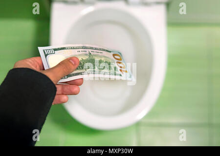 Spülen Geld in die Toilette, wirft Dollarscheine in der Toilette, Verlust Konzept, Nahaufnahme, selektive konzentrieren. Konzept der sinnlose Verschwendung von Geld, Verlust, uns
