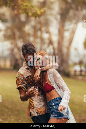 Hippie Paar, das Spaß an der Musik Festival. Mann mit einem Glas Bier seine Freundin umarmen an einem Park. Stockfoto