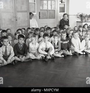 1964, historische, Gruppe der Grundschüler zusammen im Inneren sitzen auf dem Boden für die Montage, England, UK. Stockfoto