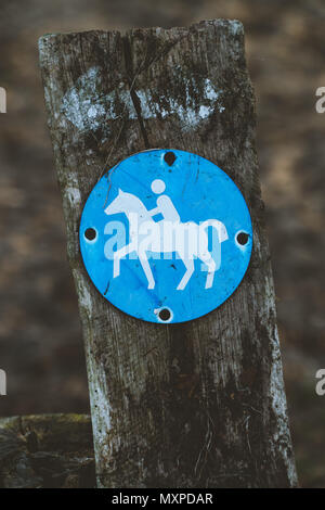 Reitweg runde blaue Zeichen auf einer hölzernen Pfahl, mit verschwommenen Land Pfad im Hintergrund. Deutschland Stockfoto