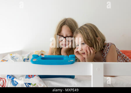 Zwei weibliche Kinder beobachten die Tablette am oberen Etagenbett Stockfoto