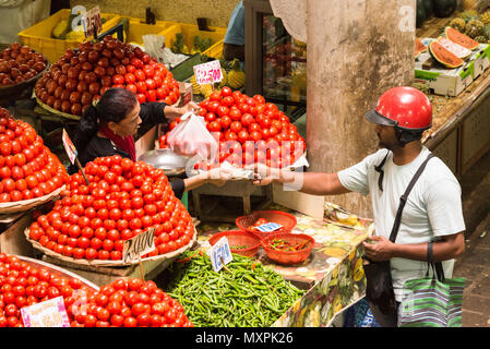 Ein Kunde in einem Motorrad helmut Zahlen für eine Plastiktüte mit Tomaten in der Obst- und Gemüsemarkt, Port Louis, Mauritius Stockfoto