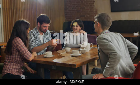 Junge schöne Menschen im Cafe Tabelle spielen name Spiel mit Aufkleber Hinweise auf Ihre Stirn geklebt. Stockfoto