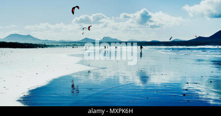 Panoramablick auf den Strand von Famara auf Lanzarote, Kanarische Inseln, Spanien, mit einigen unkenntlich Schwimmer und Kitesurfer im Hintergrund, in der Rückseite Stockfoto