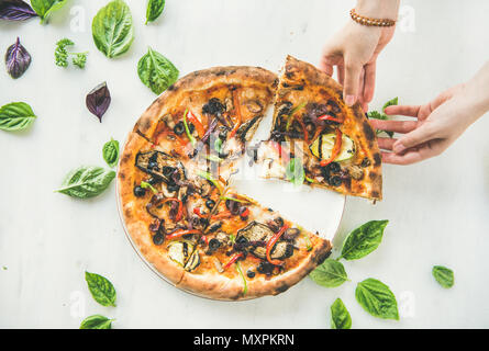 Im Sommer Mittag- oder Abendessen. Flachbild-lay von weiblichen Händen, frisch gebackene italienische vegetarische Pizza mit Gemüse und frischem Basilikum über weißem Marmor tisch Stockfoto