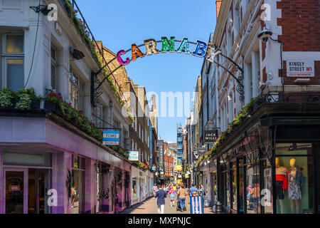 Glitzernde, bunte Schild am Eingang und Käufer in der berühmten Fußgängerzone in der Carnaby Street im West End, Soho, London W1 an einem sonnigen Tag