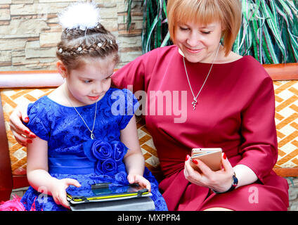 Auf dem Sofa saß die Mutter und Tochter. Das Baby in den Händen eines Tablet-PCS und Handy meiner Mutter. Stockfoto