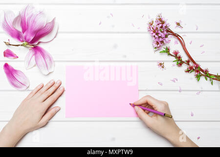 Weiße Schiff deck Tischplatte Szene mit weibliche Hände Schrift auf rosa Papier mit Pink Magnolia Blumen Stockfoto