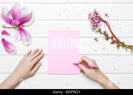 Weiße Schiff deck Tischplatte Szene mit weibliche Hände Schrift auf rosa Papier mit Pink Magnolia Blumen Stockfoto