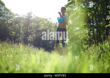 Low Angle Shot eines athletischen jungen kaukasischen Frau läuft durch ein Feld im Frühling Sonnenschein trägt einen schwarzen Leggings und Fitness Top Stockfoto