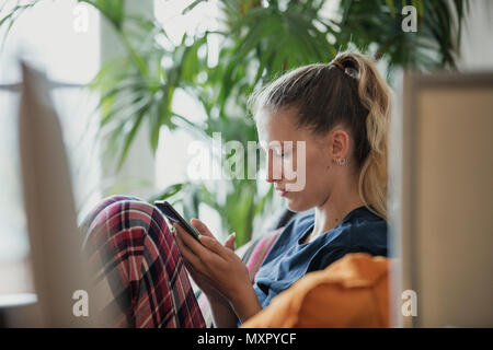 Seitenansicht eines jungen weiblichen Erwachsenen Sitzen, Relaxen, können Sie über Ihr Mobiltelefon. Stockfoto