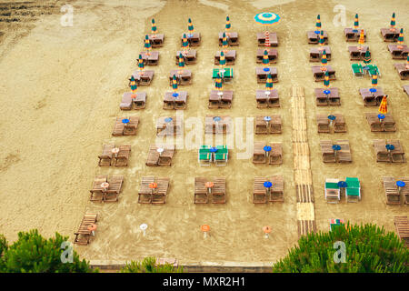 Luftbild zum Sandstrand der Adria in Albanien, voll mit Sonnenschirmen und Liegen, der Hafen von Durres in Horizont Stockfoto