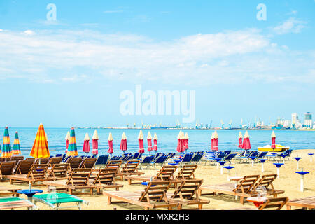 Luftbild zum Sandstrand der Adria in Albanien, voll mit Sonnenschirmen und Liegen, der Hafen von Durres in Horizont Stockfoto