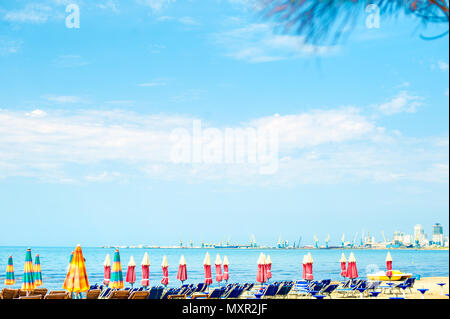 Luftbild zum Sandstrand der Adria in Albanien, voll mit Sonnenschirmen und Liegen, der Hafen von Durres in Horizont Stockfoto