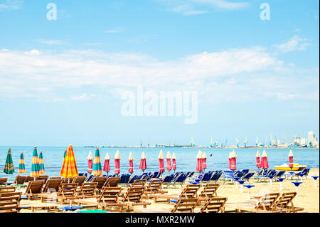 Luftbild zum Sandstrand der Adria in Albanien, voll mit Sonnenschirmen und Liegen, der Hafen von Durres in Horizont Stockfoto