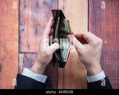 Geld in der Brieftasche, ein Mann im Anzug an einem Tisch, hält eine Brieftasche in der Hand, ein Geschäftsmann Stockfoto